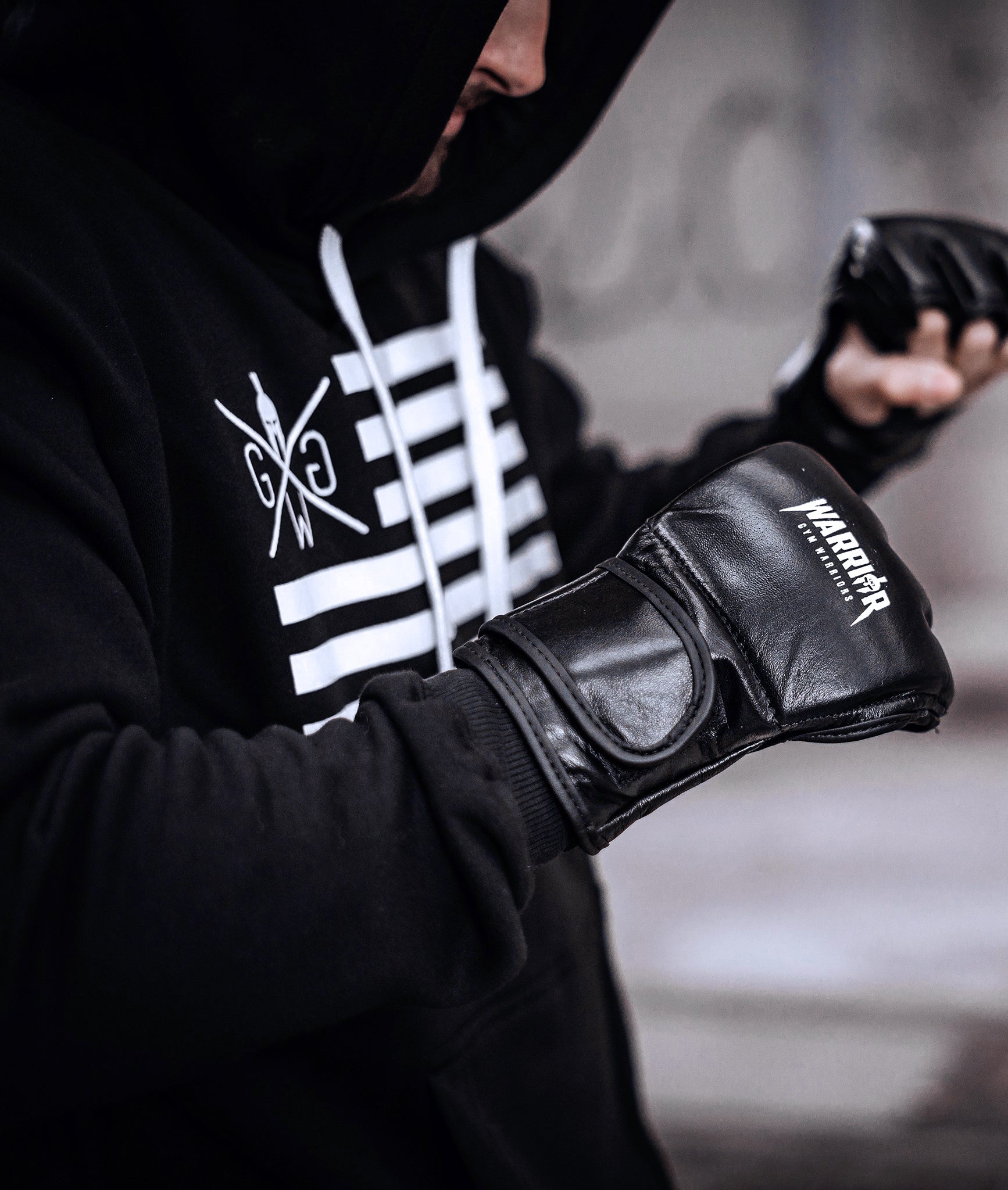 Sportler trägt schwarzen Gym Generation Hoodie mit weißem Gym Generation Print und zieht schwarze 'Warrior'-Trainingshandschuhe an.