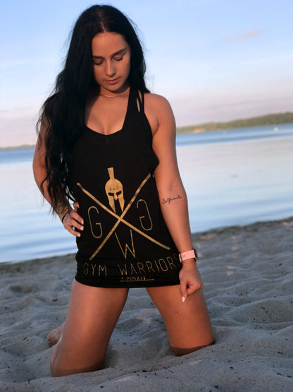 Schwarzes Stringer Tank Top mit goldenem Gym Warriors Print, getragen von weiblichen Model am Strand – perfekt für Fitness, Freizeit und sommerlichen Style.