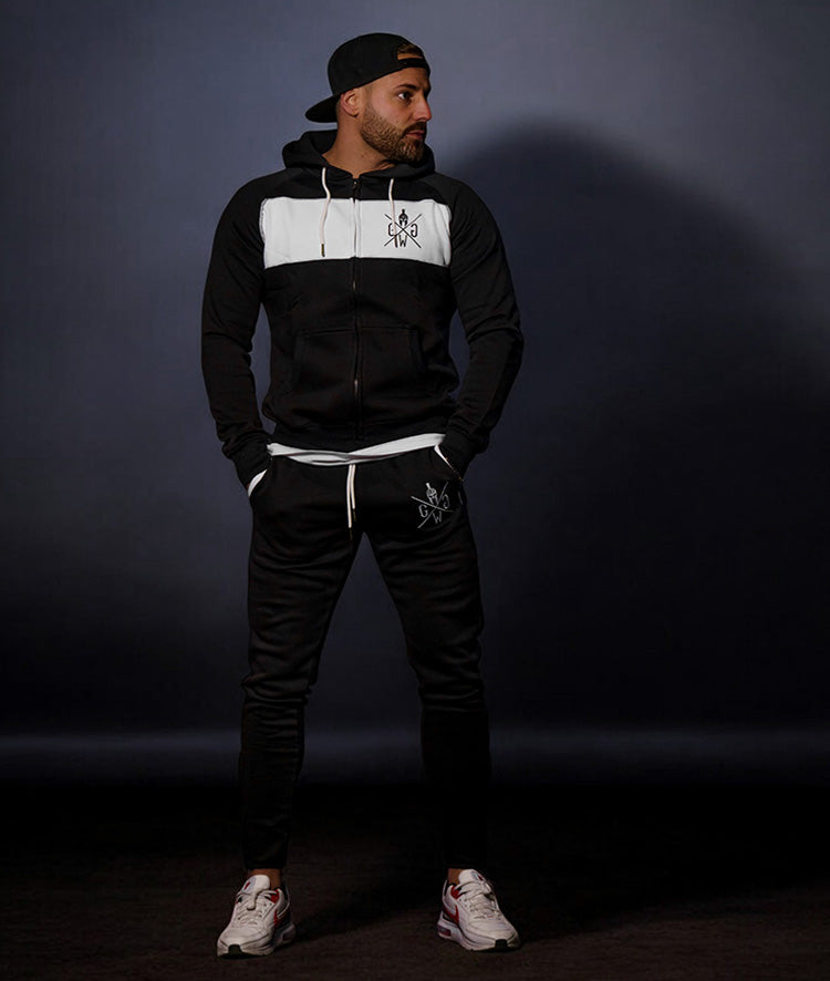 Mann in schwarzer und weißer Gym Generation Zip-Jacke und passenden Jogginghosen mit Logo, kombiniert mit Sneakers und einer Baseballmütze, ideal für Sport und Freizeit.