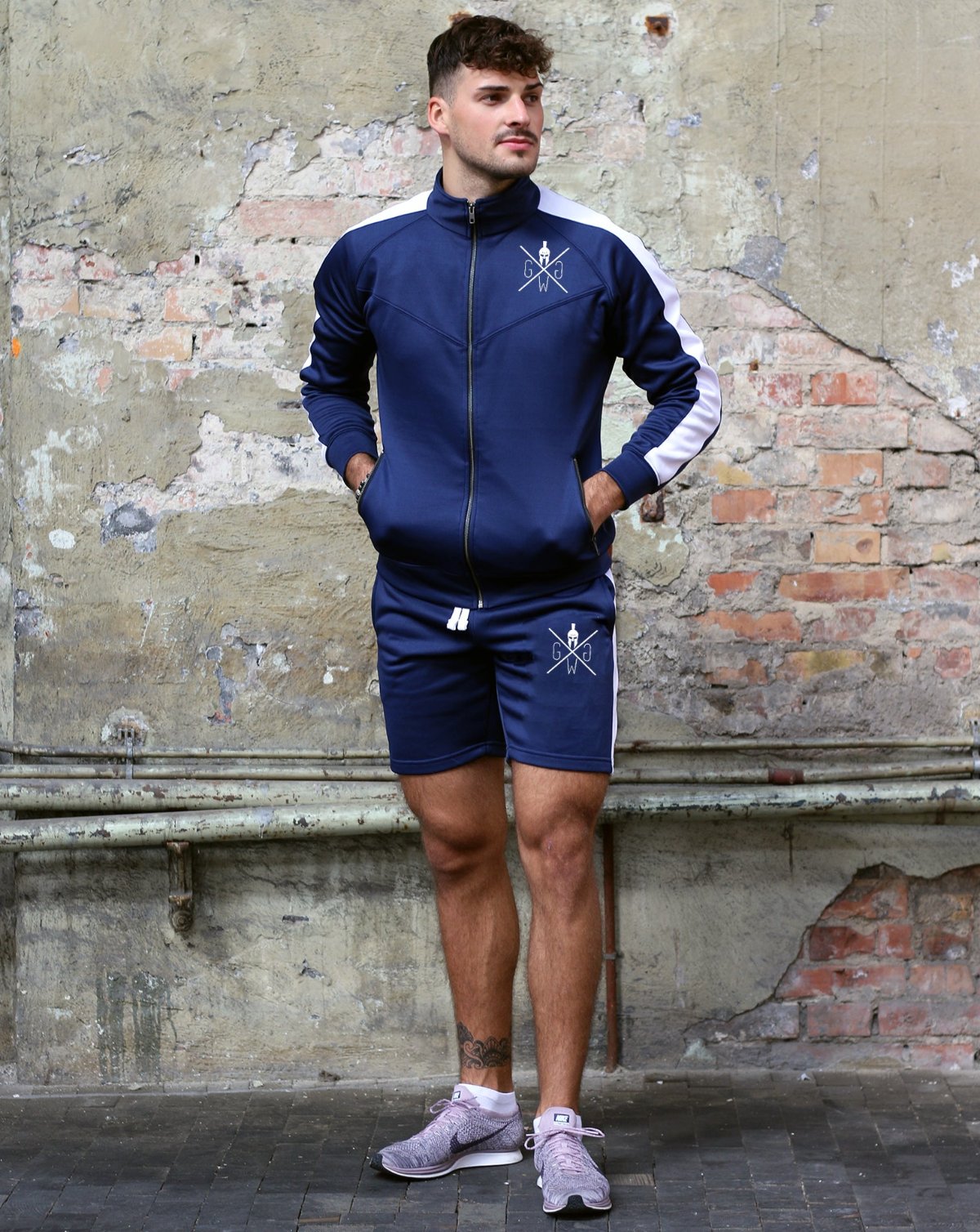 Athlet in dunkelblauem Trainingsanzug mit weissen Streifen, bestehend aus einer Jacke und Shorts mit Gym-Generation-Logo