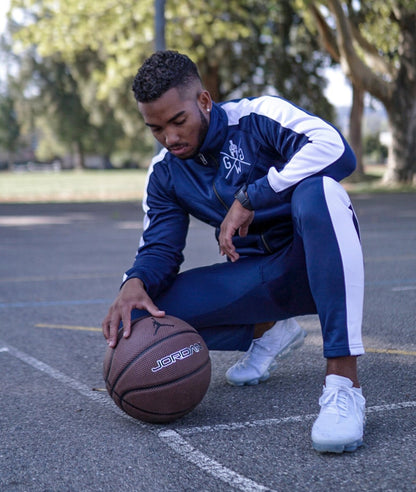 Dunkelblaue Gym Generation Trainingsjacke und Sporthose mit weissen Streifen. Model: Smart Santi in Miami