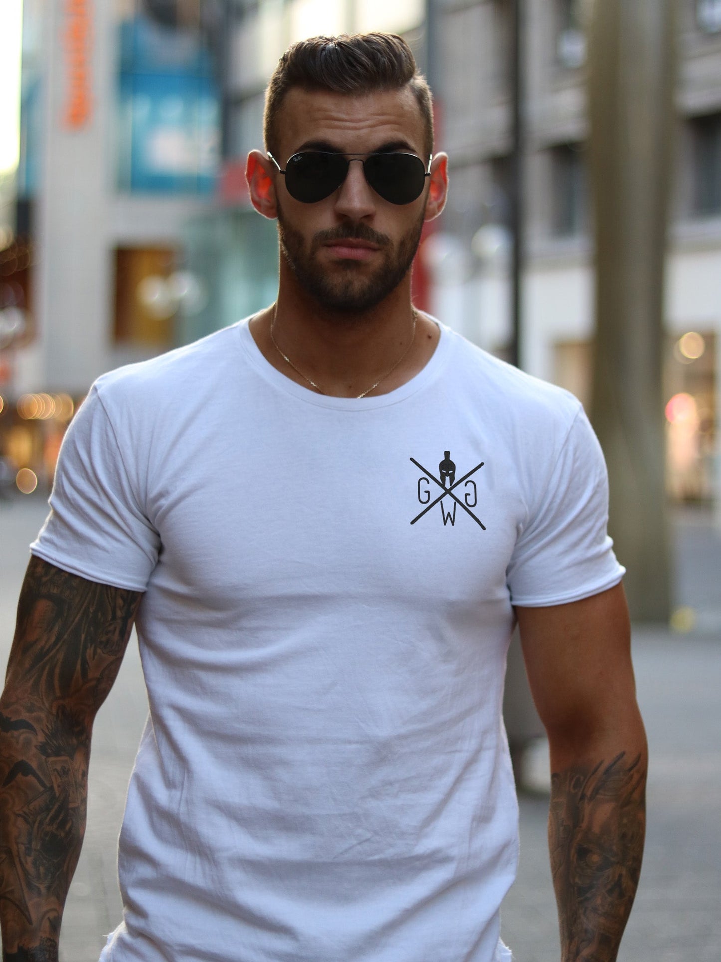 Mann trägt das Gym Generation Gym T-Shirt in Weiß mit Spartaner-Logo auf der Brust, in einem modernen Streetstyle-Look in der Stadt.