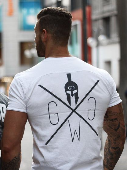 Mann in einem weißen Gym Generation T-Shirt mit Spartaner-Logo auf dem Rücken, getragen in einer urbanen Straßenszene.