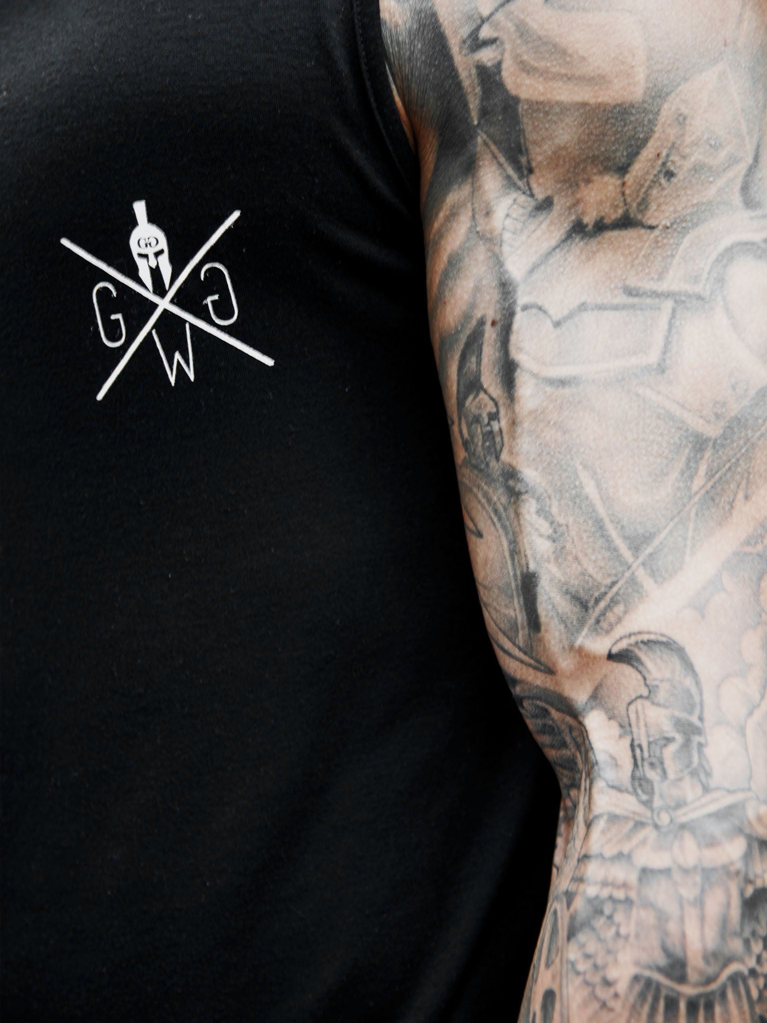 Nahaufnahme des Gym Generation Muscle Tank Tops in Schwarz, zeigt das dezente Logo-Detail auf der Brust.